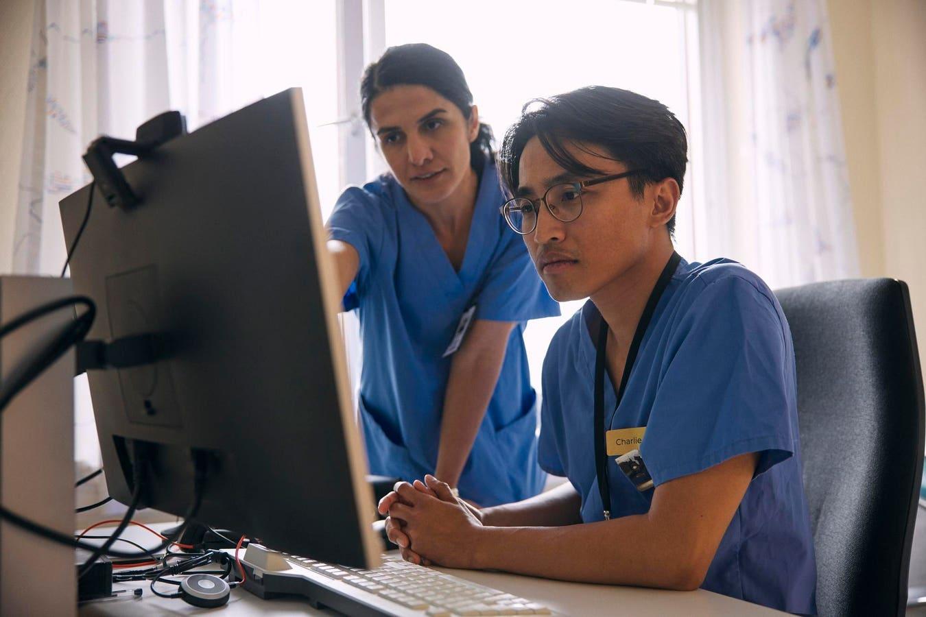 Two clinicians in scrubs reviewing a screen together